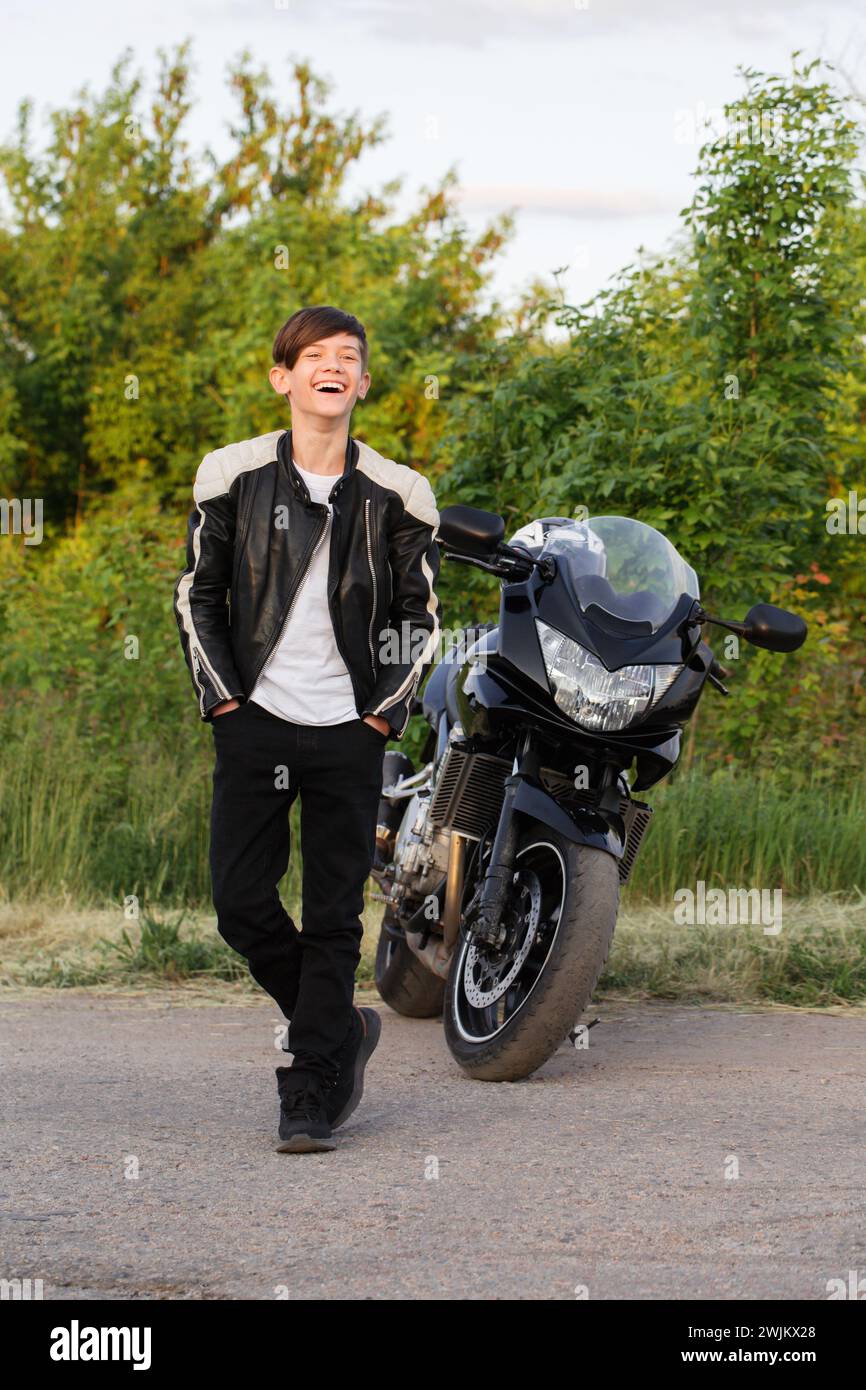 Un ragazzo adolescente ride allegramente vicino a una moto Foto Stock
