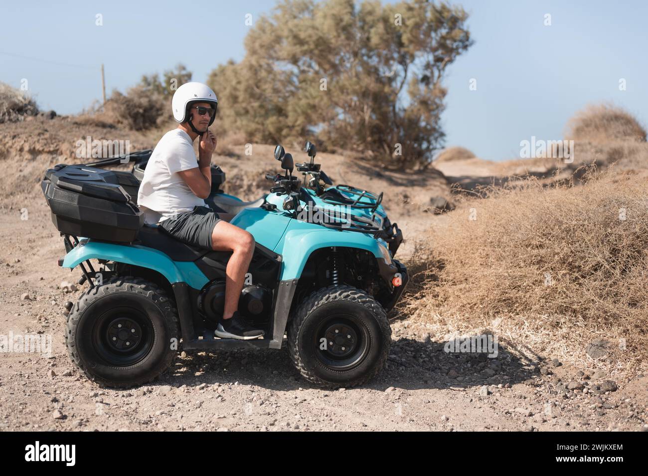 Giovane che si assicura il casco su un atv a quattro ruote su pista fuoristrada Foto Stock