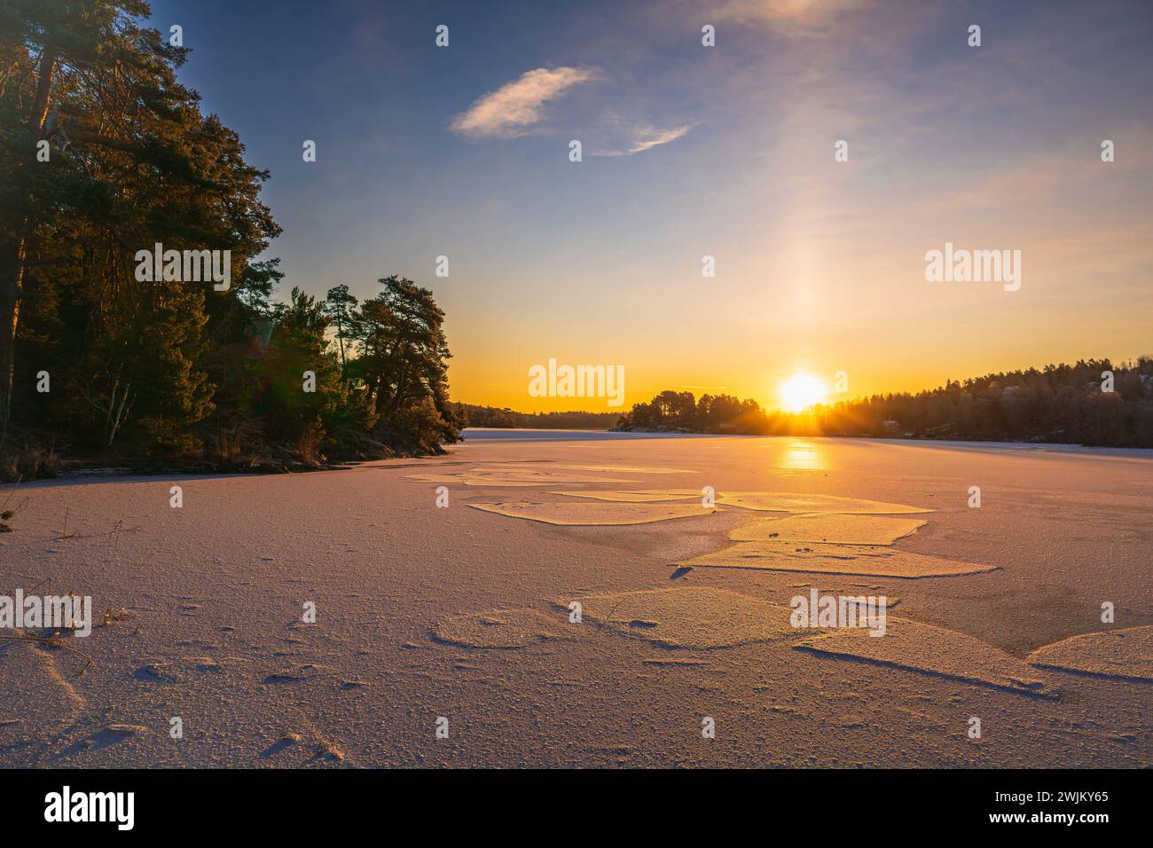 Alba di un lago ghiacciato, con cielo azzurro, sottile strato di cirrus, tardo inverno svedese, vicino a Drottningholm, Stoccolma. Foresta e alberi. Foto Stock