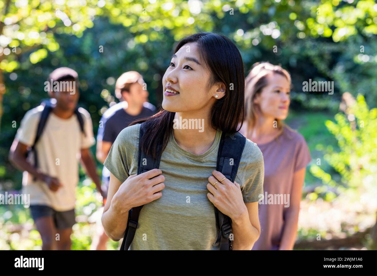 Giovane donna adulta curiosa che guarda in alto mentre fa trekking con gli amici Foto Stock