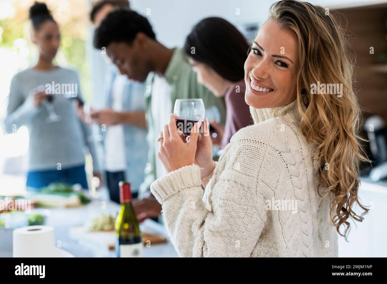Allegra donna adulta che guarda indietro la macchina fotografica mentre tiene in mano wineglass Foto Stock