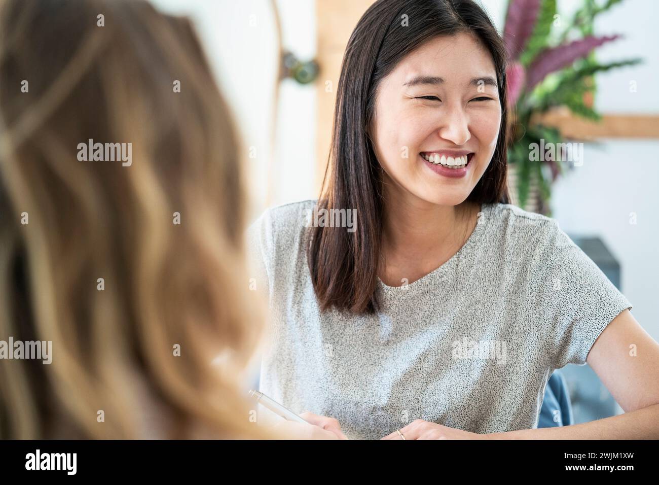 Donna allegra seduta alla scrivania mentre tiene la penna Foto Stock