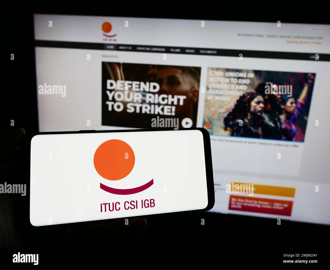 Persona che detiene un cellulare con il logo della federazione della Confederazione sindacale internazionale (ITUC) davanti alla pagina web. Mettere a fuoco il display del telefono. Foto Stock