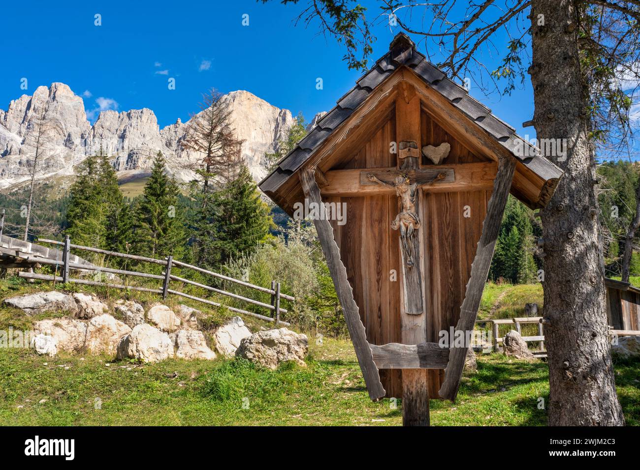 Santuario in legno con statua di gesù di fronte al massiccio del Rosengarten, Dolomiti, italia. Bel cielo blu. Foto Stock