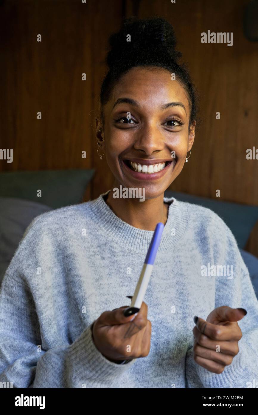 Giovane donna adulta sorridente alla telecamera mentre tiene un test di gravidanza Foto Stock