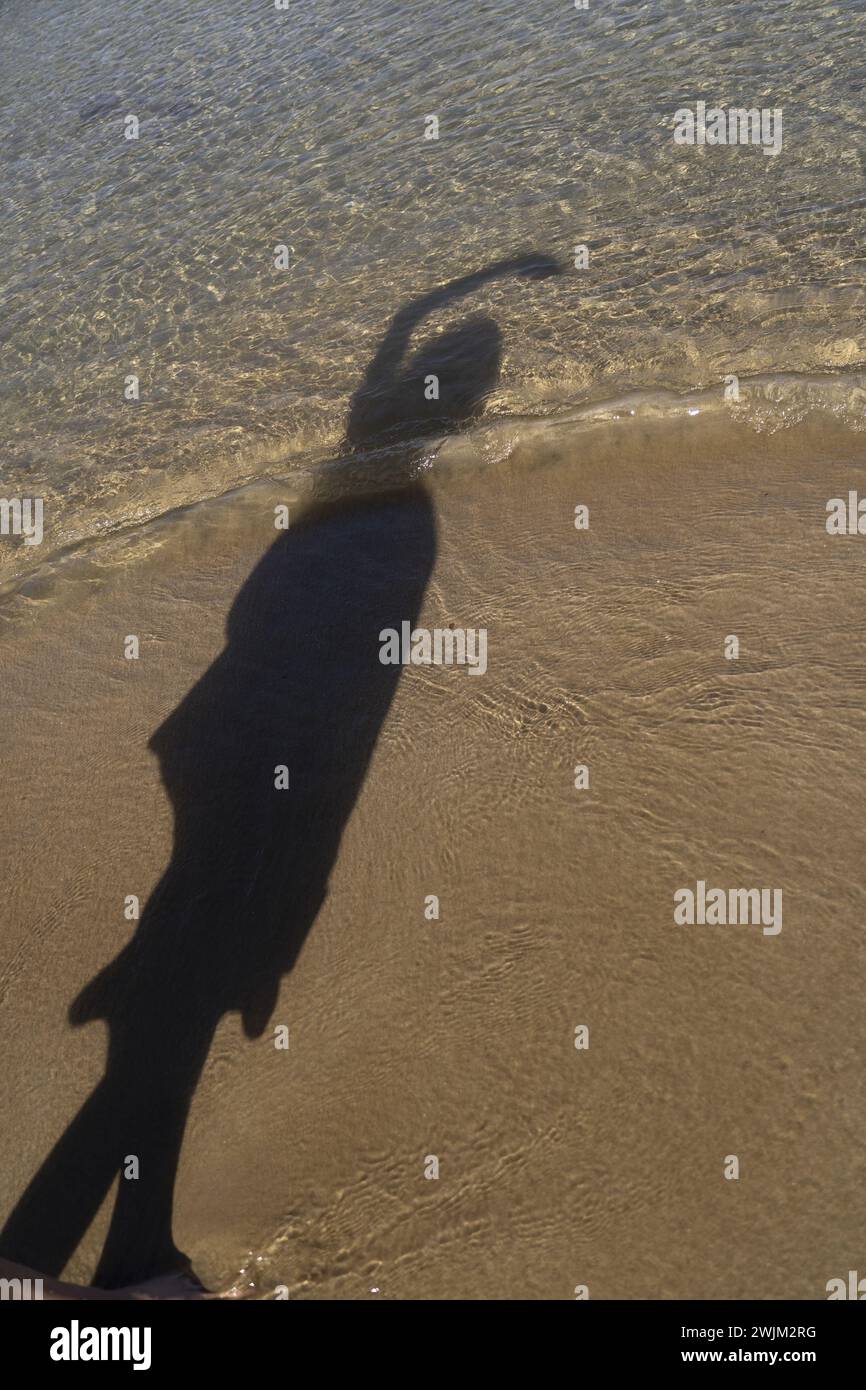 Ombra di una persona non identificata sulla spiaggia sabbiosa vicino al bordo dell'acqua Foto Stock