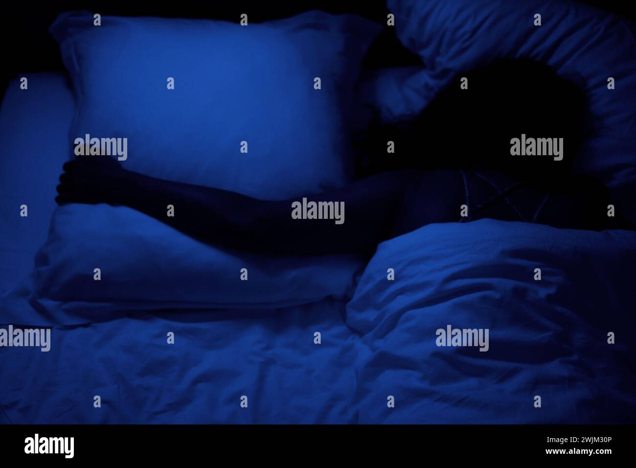 Colpo di persona poco illuminato che abbraccia il cuscino mentre dorme Foto Stock
