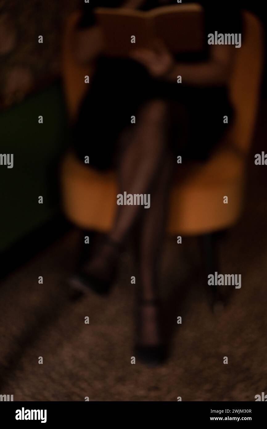 Foto sfocata della metà inferiore della donna seduta su una sedia nella stanza buia Foto Stock