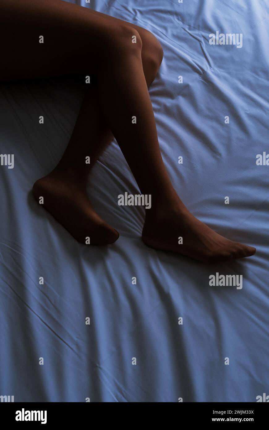 Gambe di una persona non identificata sdraiate a letto Foto Stock