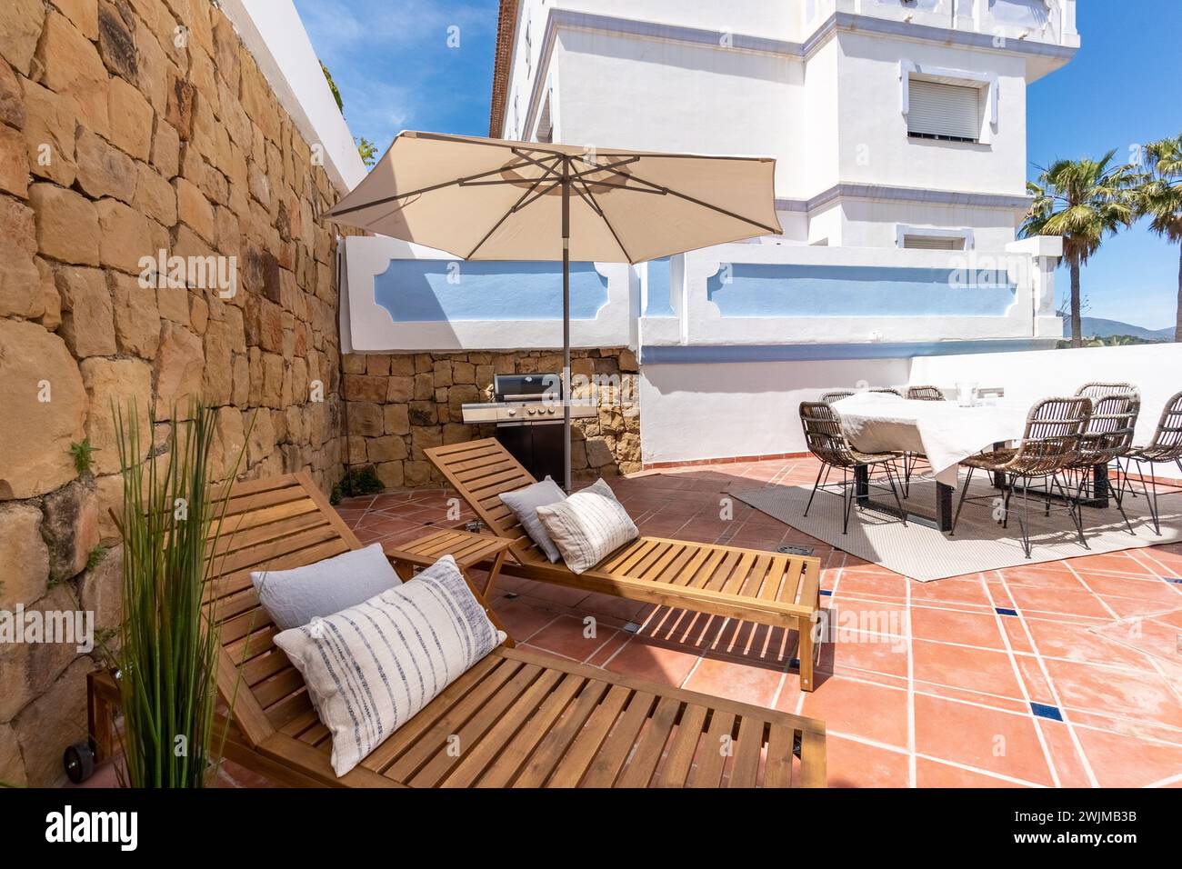 una lussuosa terrazza giardino piena di sedie a sdraio e tavolo da pranzo, area barbecue in appartamenti mediterranei Foto Stock