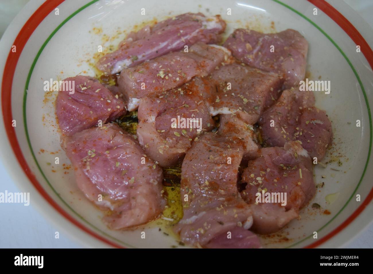 Pezzi di filetto di maiale crudo marinati in una ciotola, pronti per essere cotti. Foto Stock