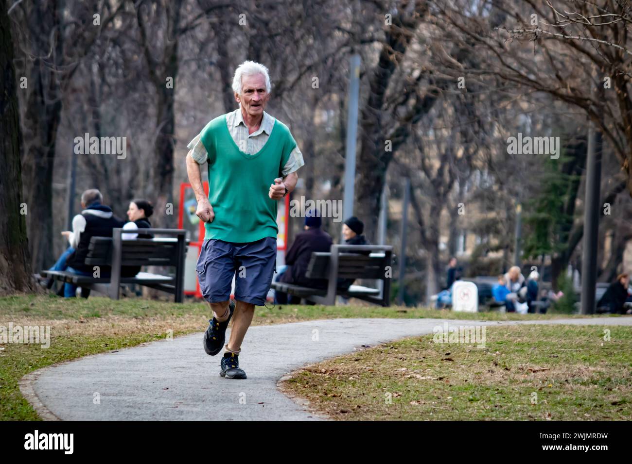 Uomo anziano che fa jogging nel parco pubblico della città la mattina, corre all'aperto, vita sana e mantenersi in forma Foto Stock