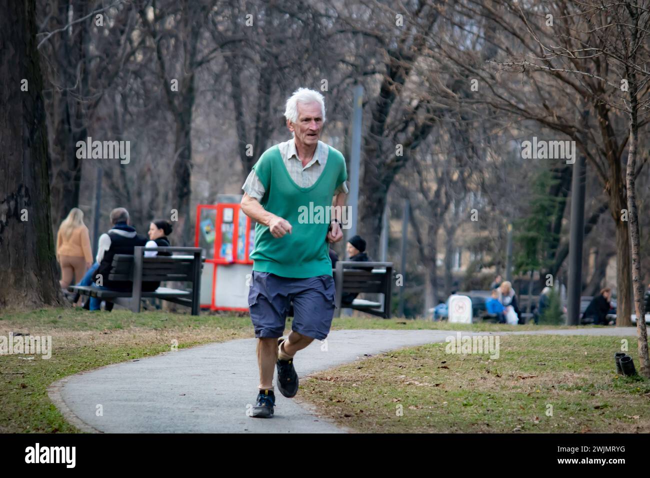 Uomo anziano che fa jogging nel parco pubblico della città la mattina, corre all'aperto, vita sana e mantenersi in forma Foto Stock