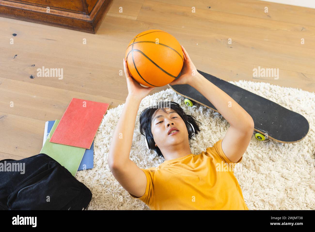 Adolescente asiatico giace sul pavimento di casa, tenendo in mano una pallacanestro Foto Stock