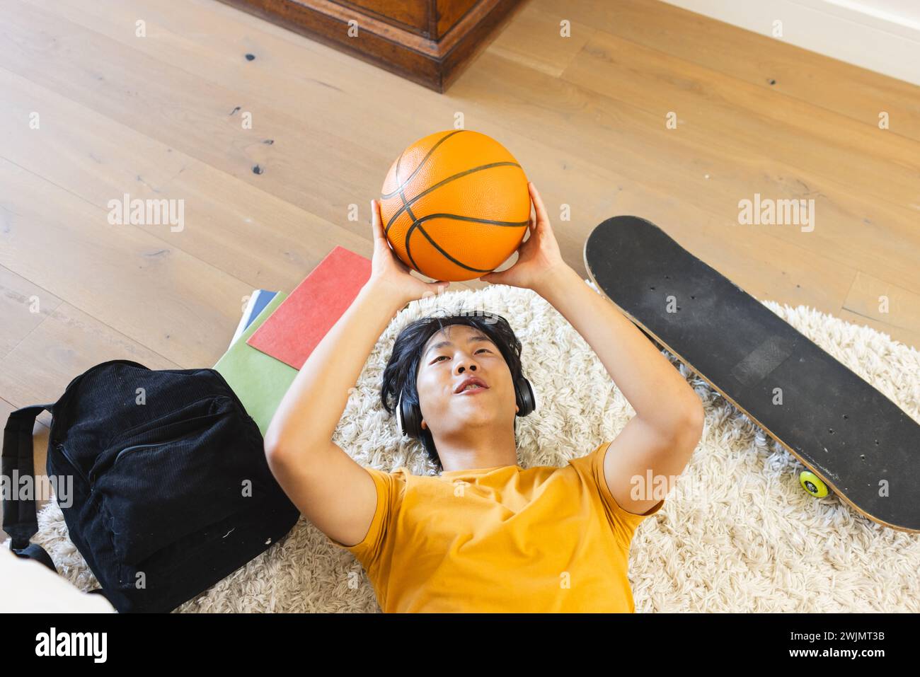 Adolescente ragazzo asiatico giace sul pavimento tenendo un basket Foto Stock