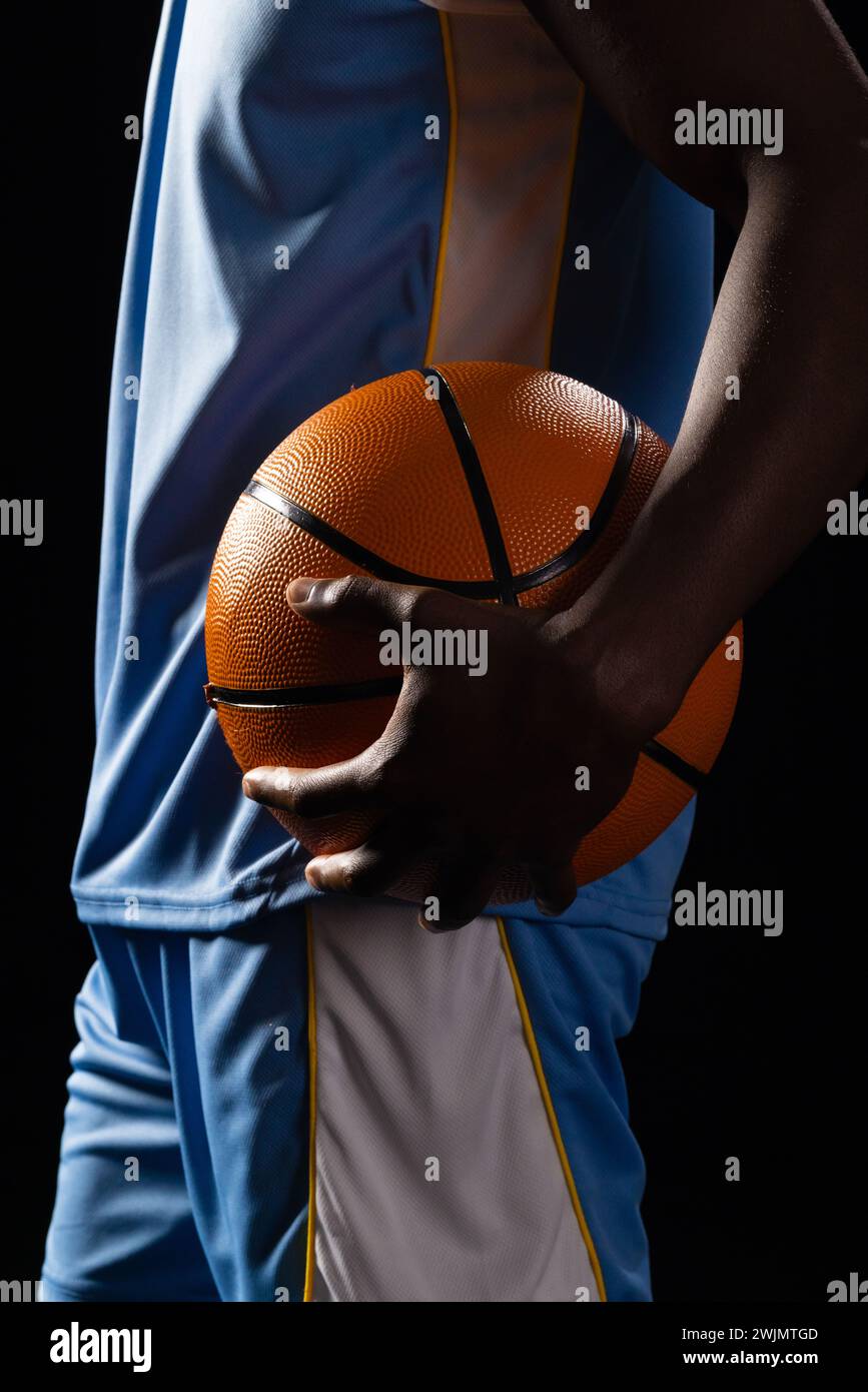 Uomo afroamericano che regge una pallacanestro su sfondo nero Foto Stock
