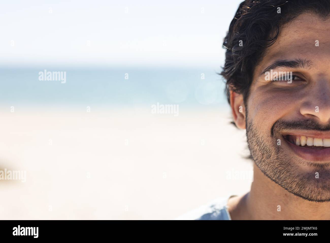 Il giovane uomo birazziale sorride brillantemente in spiaggia, con spazio per copiare Foto Stock