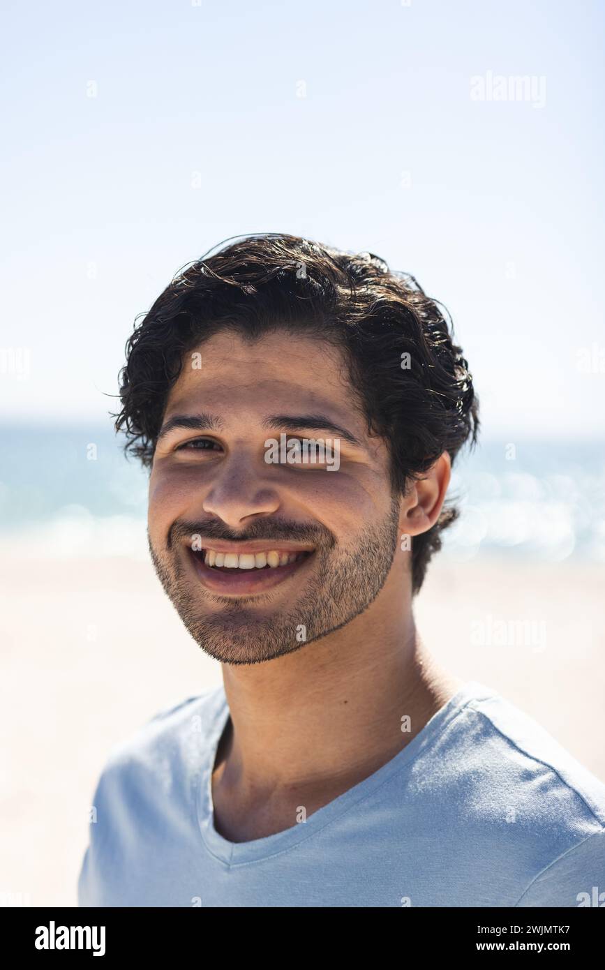 Il giovane uomo birazziale sorride brillantemente in spiaggia Foto Stock