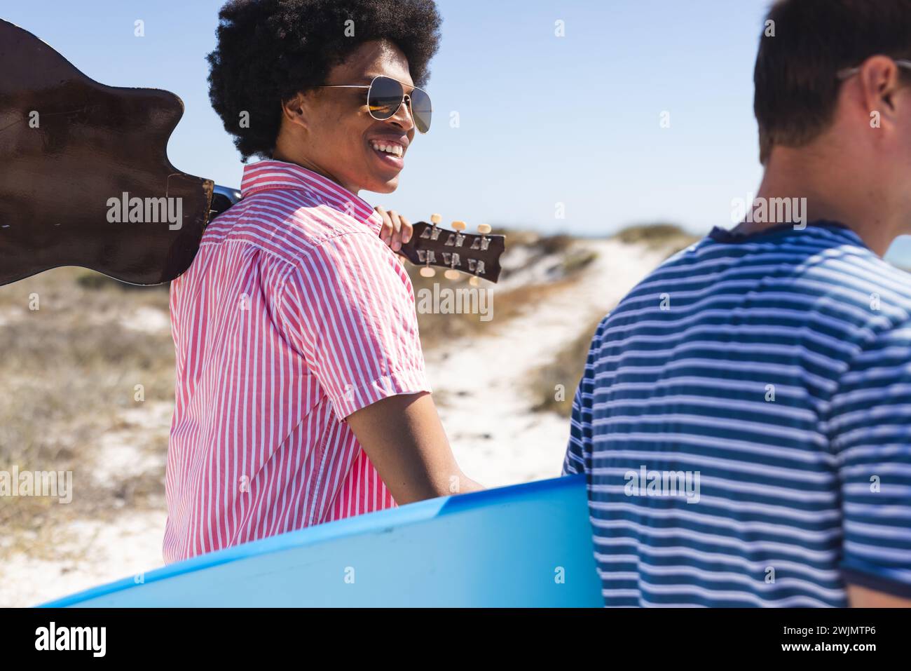 Amici diversi si godranno una rilassante jam session sulla spiaggia condotta da un chitarrista. Foto Stock