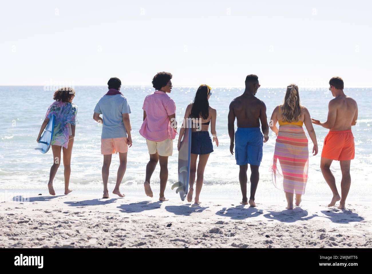 Un gruppo eterogeneo di amici ama trascorrere una giornata in spiaggia, creando una vivace scena all'aperto in riva all'oceano Foto Stock