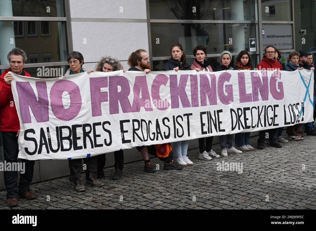 Kassel, Germania. 16 febbraio 2024. Gli attivisti per il clima manifestano contro il terminale GNL di Rügen con uno striscione che recita "No fracking LNG - il gas naturale pulito è una bugia sporca!" Di fronte alla sede centrale del gestore della rete del gas Gascade. Gli attivisti hanno criticato il terminal sull'isola del Mar Baltico e l'ulteriore espansione delle infrastrutture di importazione di GNL in Germania come un crimine climatico. Crediti: Uwe Zucchi/dpa/Alamy Live News Foto Stock