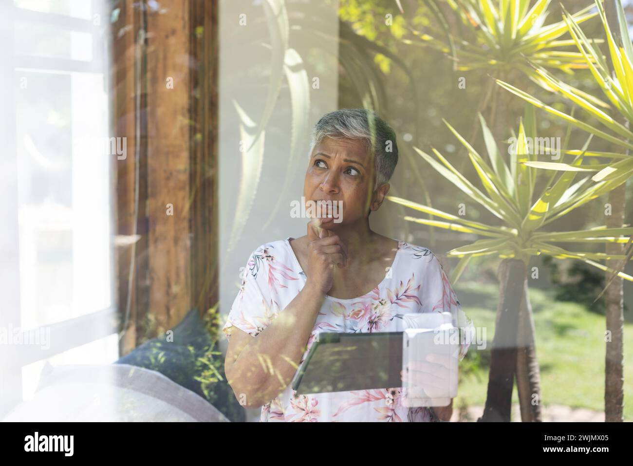 Una donna birazziale matura guarda fuori da una finestra a casa, con spazio di copia Foto Stock