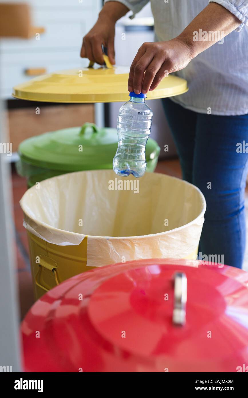 Una donna birazziale matura che ricicla una bottiglia di plastica a casa, con spazio per le copie Foto Stock