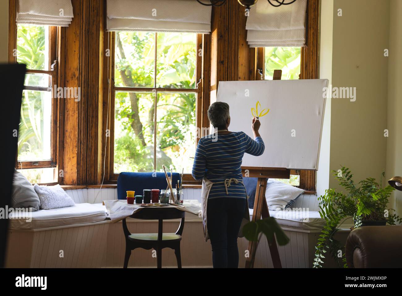 Un'artista birazziale matura dipinge su una tela a casa, con spazio di copia Foto Stock