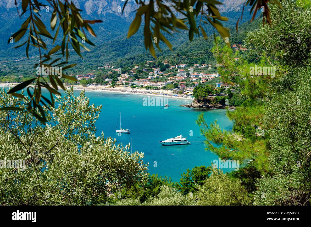 Alcune barche navigano tra una vegetazione lussureggiante e maestose montagne a Thassos Foto Stock
