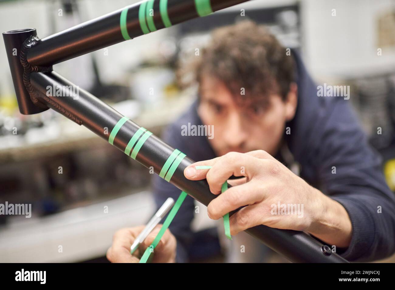 Processo creativo di preparazione del telaio di una bicicletta con nastro di mascheratura per un disegno di verniciatura personalizzato in un'officina di biciclette. Composizione selettiva della messa a fuoco. Foto Stock