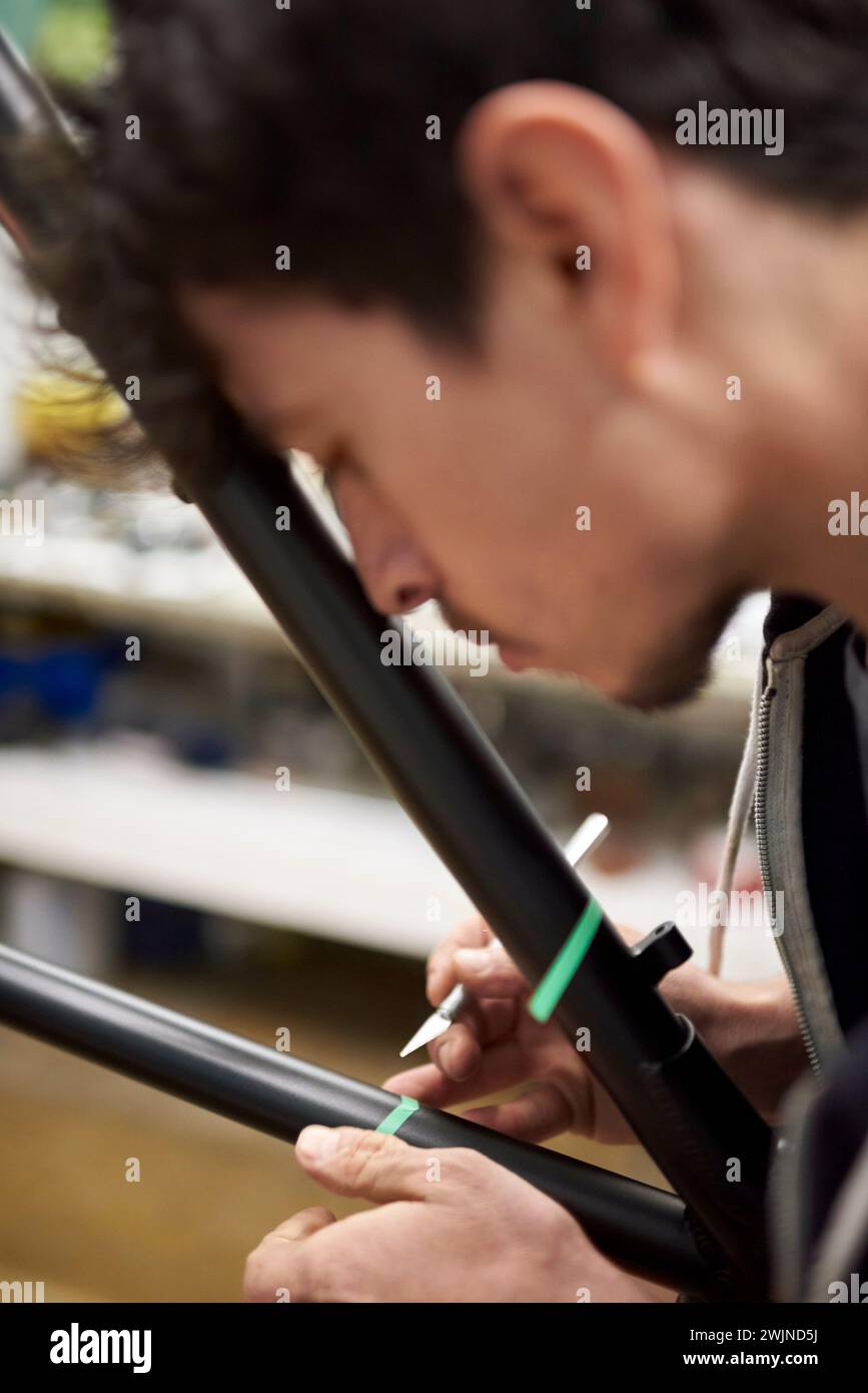 Il giovane ispanico si è concentrato sulla preparazione di un telaio per bicicletta con bisturi e nastro di mascheratura per un disegno di pittura personalizzato nella sua officina di bici, un'opera artigianale Foto Stock