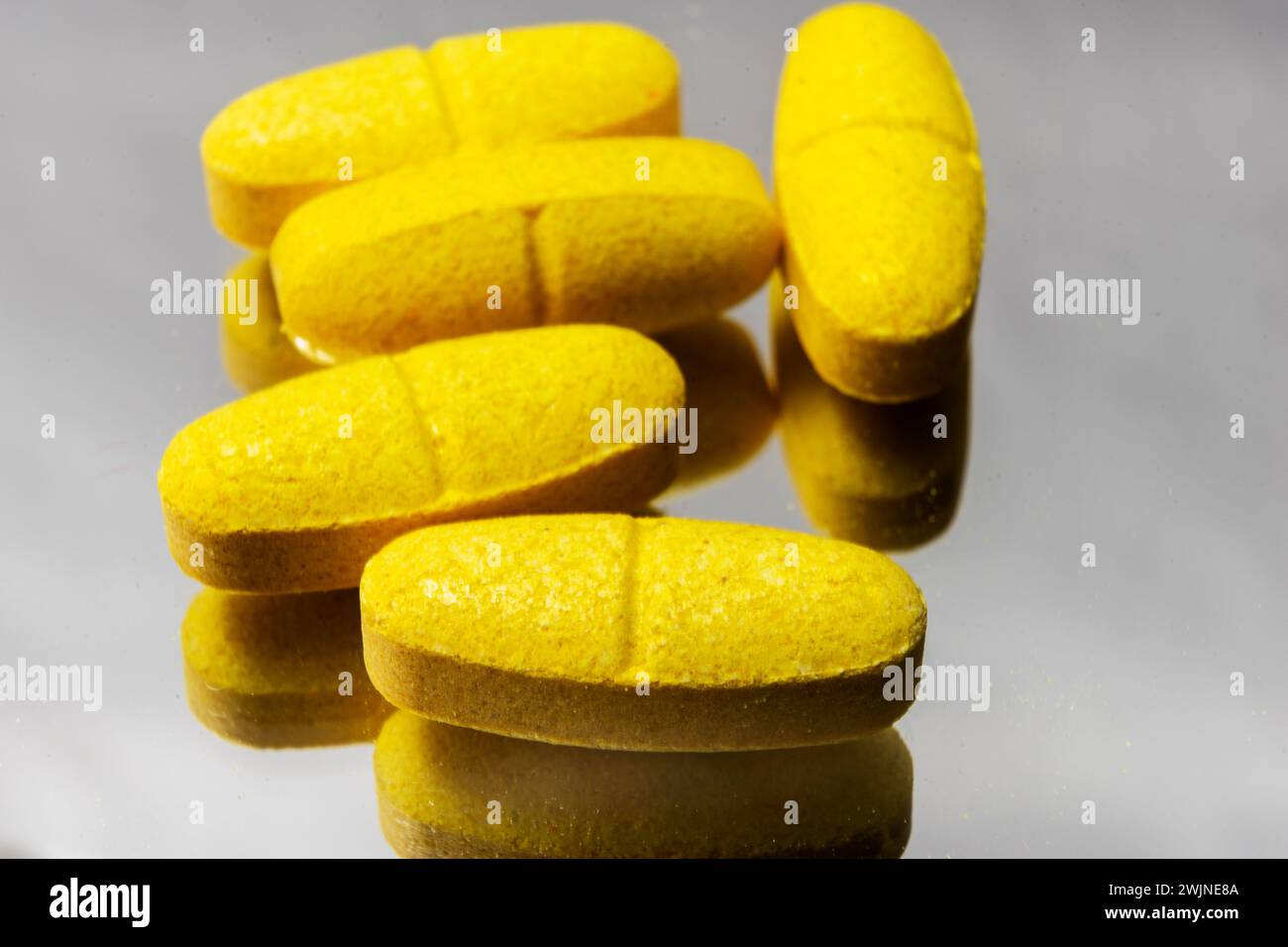 pillole vitaminiche gialle su sfondo grigio con riflesso Foto Stock