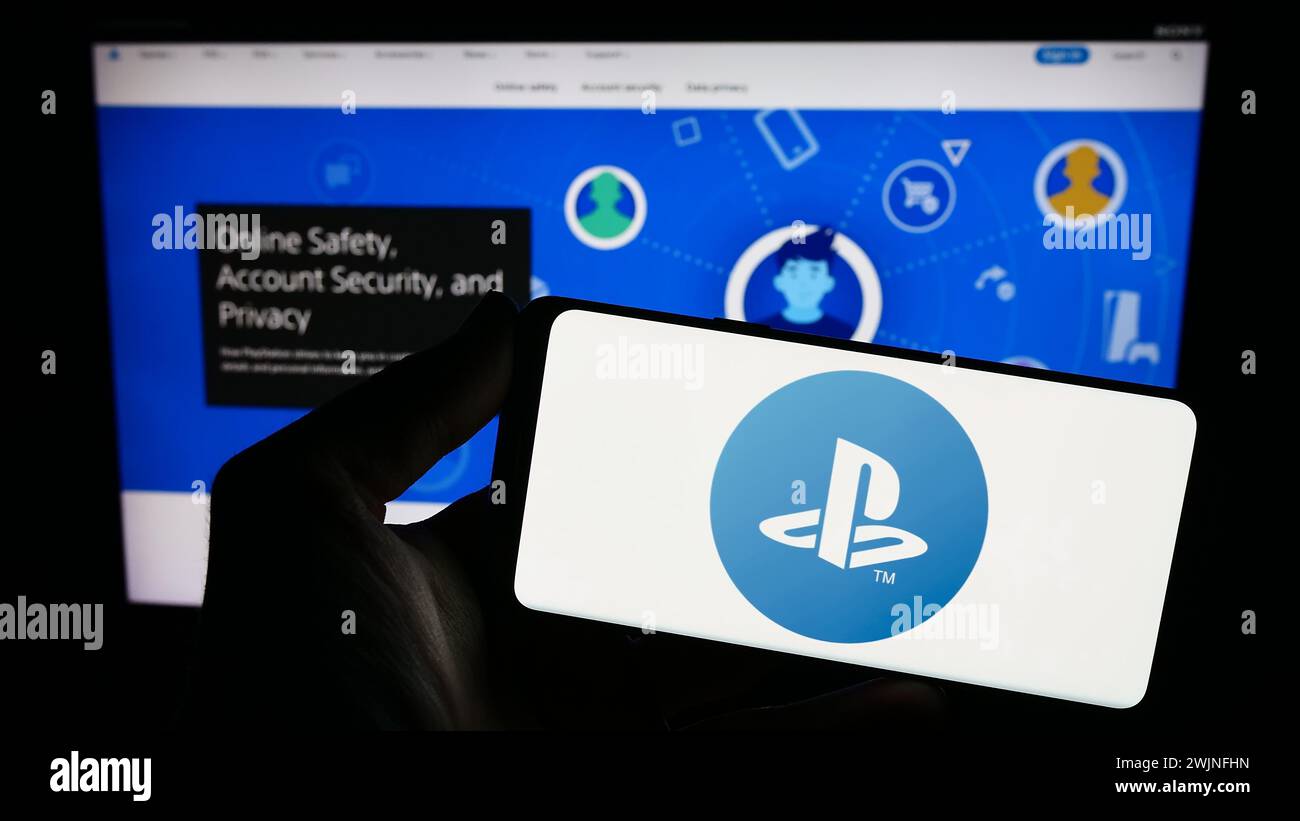 Persona con smartphone e logo della piattaforma di videogiochi PlayStation Network (PSN) davanti al sito Web. Mettere a fuoco il display del telefono. Foto Stock