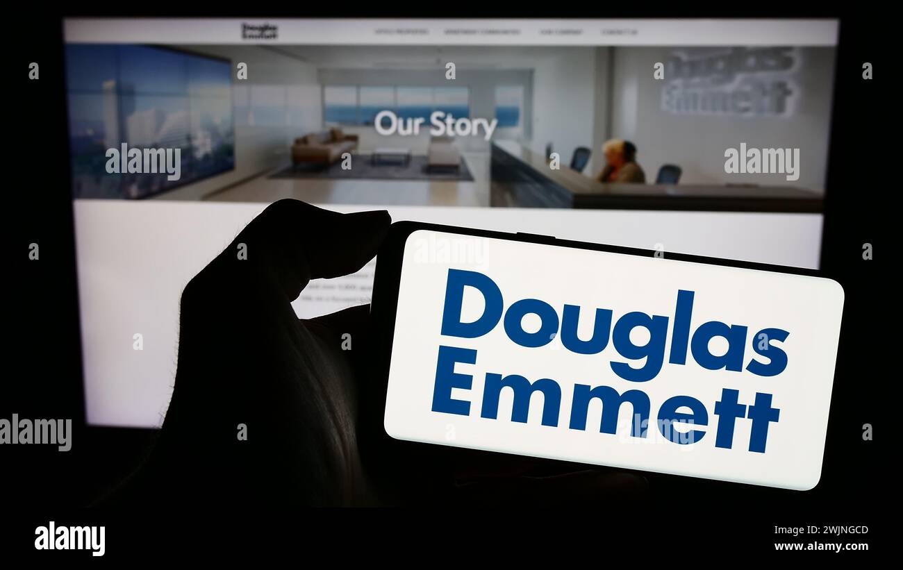 Persona che possiede uno smartphone con il logo della società immobiliare statunitense Douglas Emmett Inc. Davanti al sito Web. Mettere a fuoco il display del telefono. Foto Stock