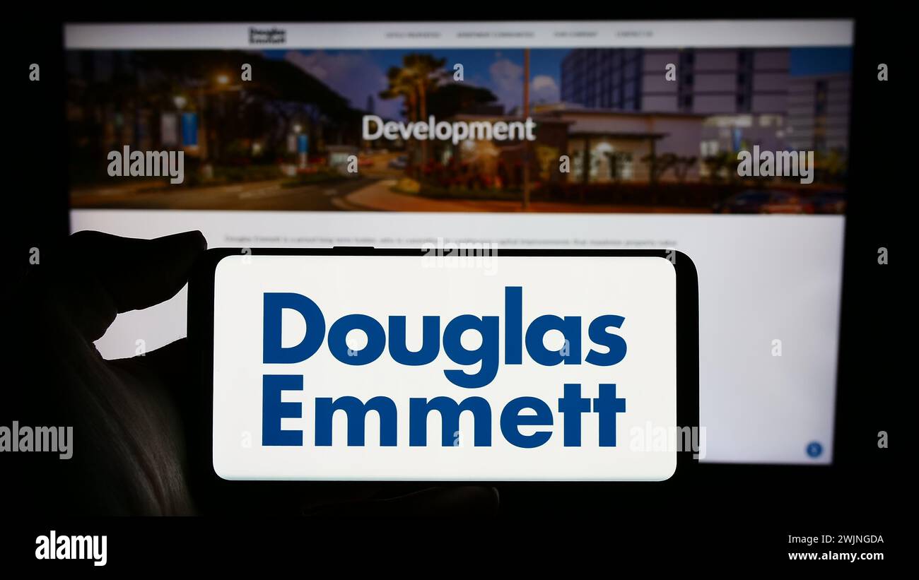 Persona che detiene un cellulare con il logo della società immobiliare statunitense Douglas Emmett Inc. Di fronte alla pagina web aziendale. Mettere a fuoco il display del telefono. Foto Stock
