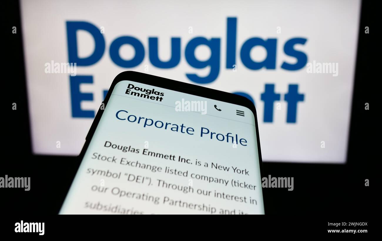 Smartphone con sito web della società immobiliare statunitense Douglas Emmett Inc. Davanti al logo aziendale. Mettere a fuoco in alto a sinistra sul display del telefono. Foto Stock