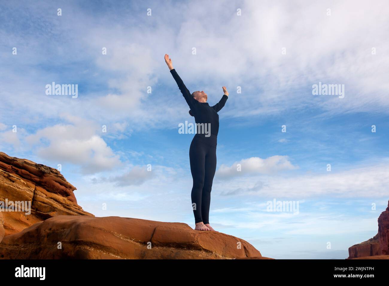 donna sportiva in piedi su rocce rosse con le braccia sollevate. Foto Stock