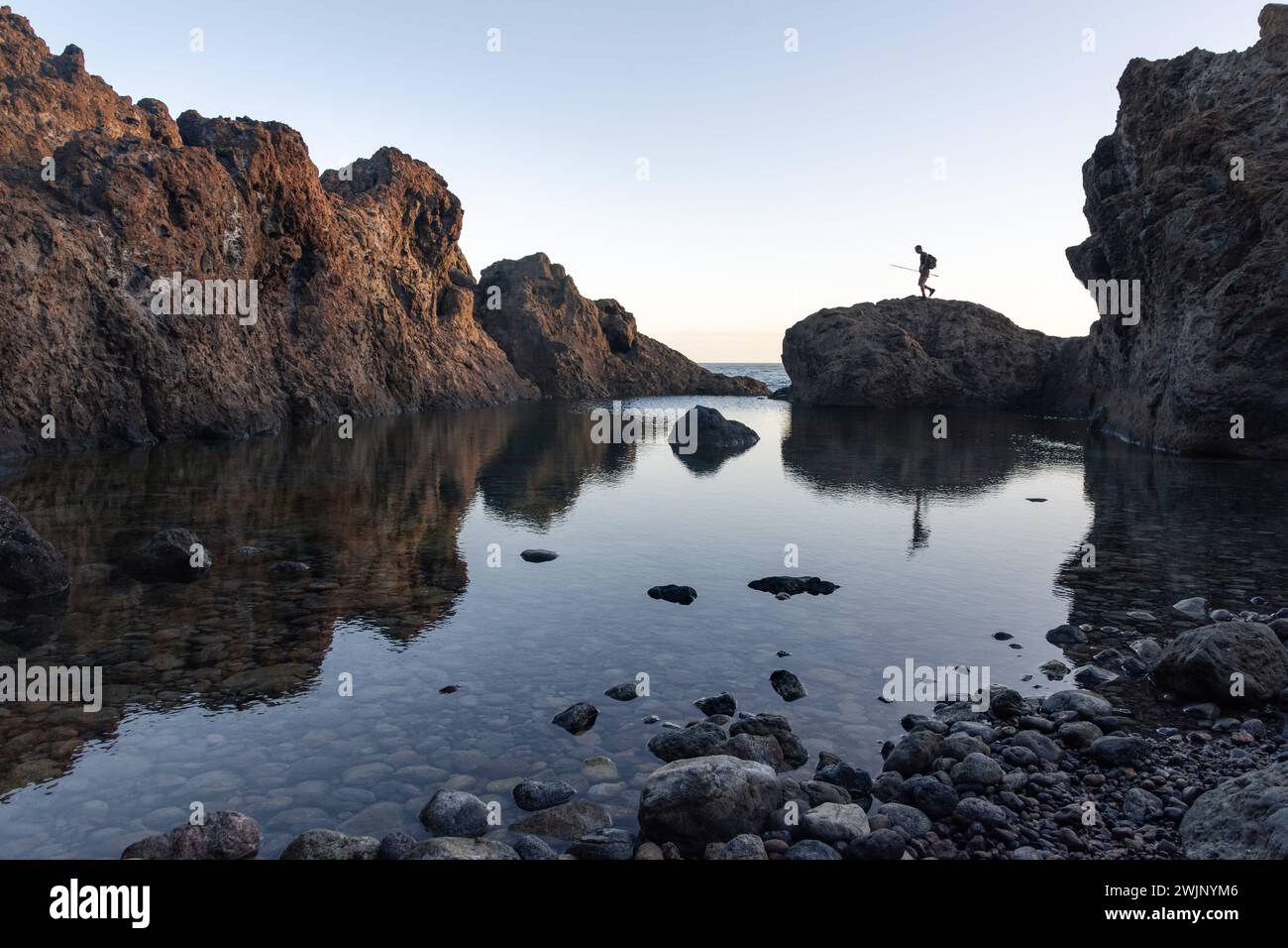 Un pescatore cammina lungo le rocce di una piscina naturale a Tenerife all'alba. Foto di alta qualità Foto Stock