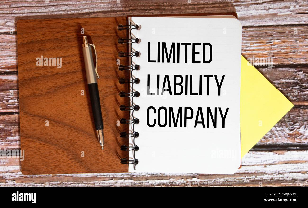 LLC- Limited Liability Company acronimo scritto in quaderno su sfondo in legno. Foto Stock