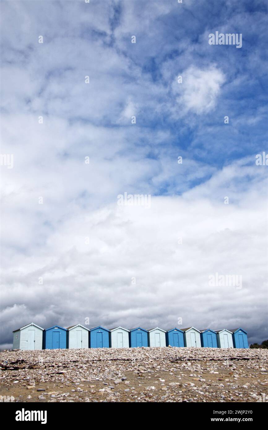 Fila di capanne sul mare britannico sotto il cielo azzurro nuvoloso dell'estate. Queste capanne erano su una spiaggia di ciottoli di un villaggio turistico nel Dorset, nel Regno Unito Foto Stock