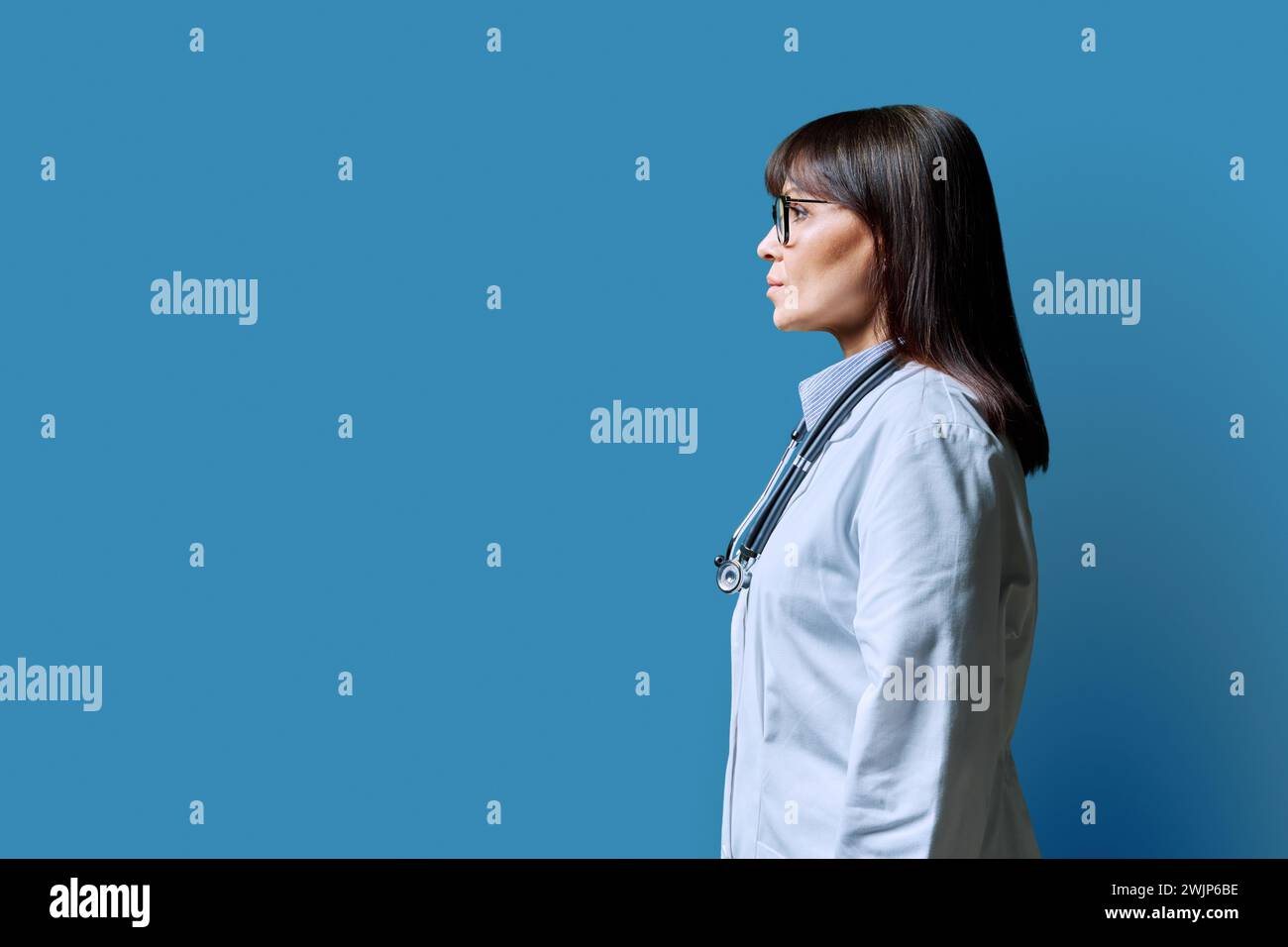 Vista profilo medico donna matura seria, sfondo blu, spazio copia Foto Stock