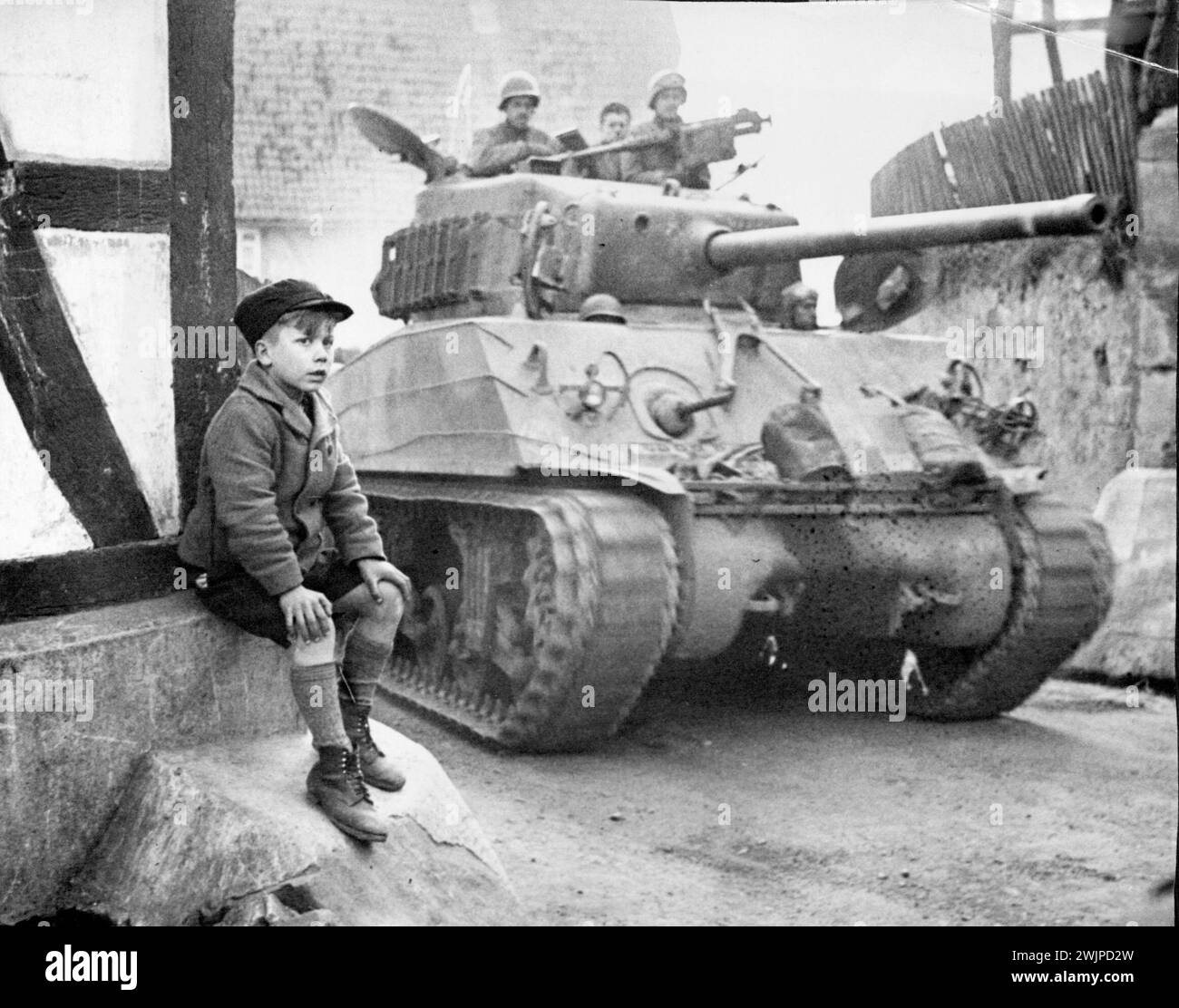 Guardate Yank Armor Roll By -- Un ragazzo tedesco siede sul lato di una strada a Zwisten, in Germania, incantato dallo spettacolo dei carri armati della nona divisione corazzata della prima Armata americana che si muovono attraverso la città. 9 aprile 1945. (Foto di William C. Allen, Associated Press Photo). Foto Stock