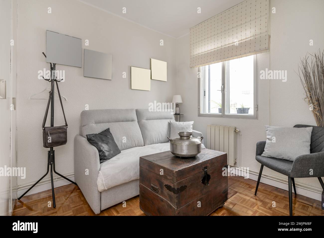 Piccolo soggiorno in una casa con mobili e accessori che combinano stile vintage e contemporaneo, pavimenti in parquet, doppie finestre in alluminio con Foto Stock