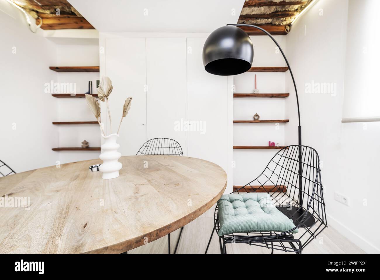 Un bellissimo appartamento loft con mobili di design contemporaneo, un tavolo rotondo con piano in legno, sedie a doghe nere e una lampada a piedi nera Foto Stock