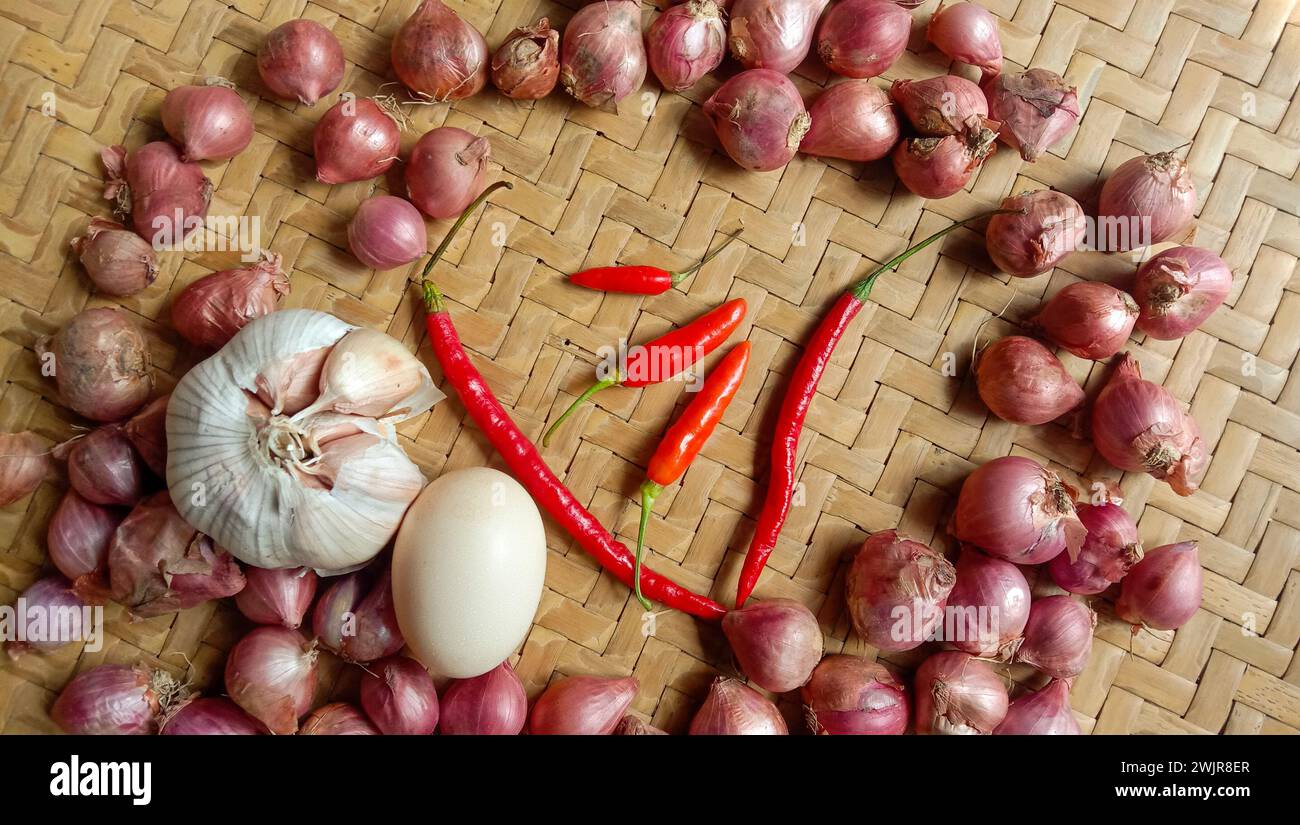 Foto di spezie sotto forma di scalogni, aglio, peperoncini e uova disposte in un bambù intrecciato Foto Stock