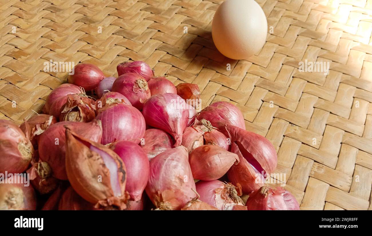 Foto di spezie sotto forma di scalogni, aglio, peperoncini e uova disposte in un bambù intrecciato Foto Stock