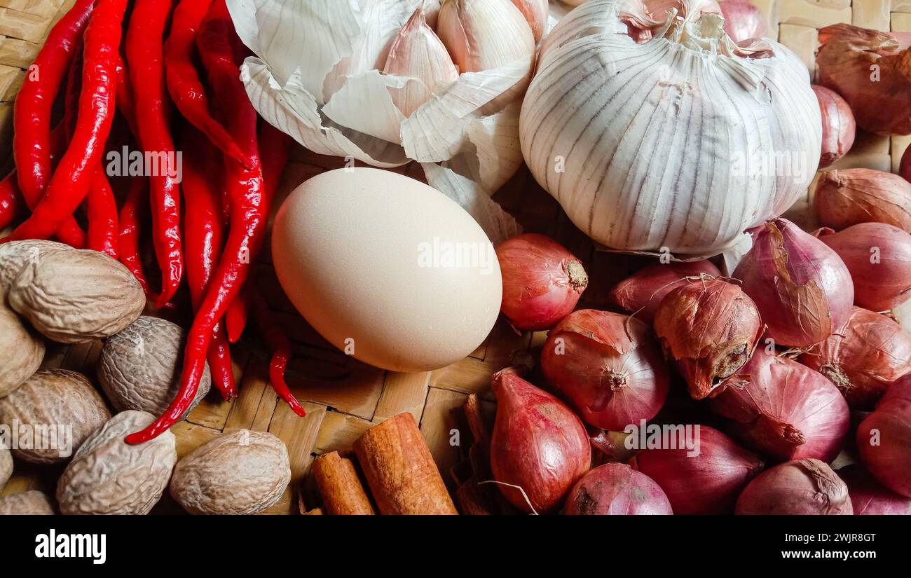 Foto di spezie sotto forma di scalogni, aglio, peperoncini e uova disposte in un bambù intrecciato Foto Stock