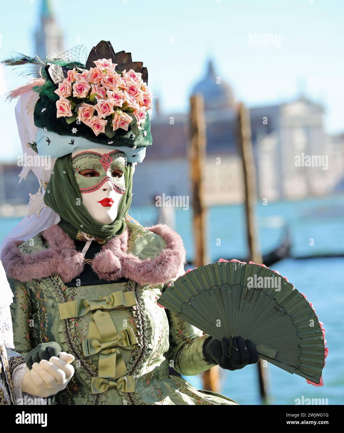 Donna in maschera durante il carnevale di Venezia in Italia con grande copricapo e ventilatore in mano Foto Stock