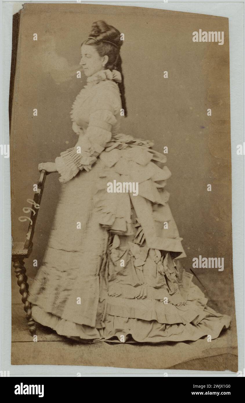 Donna di profilo con un vestito chiaro, sostenuta da una sedia. 1870-1875. Fotografia anonima. Galliera, museo della moda della città di Parigi. 60251-17 sedia, acconciatura, falsificazione, donna, moda femminile, modello, stand, secondo impero, xix secolo, vestito, bagno Foto Stock