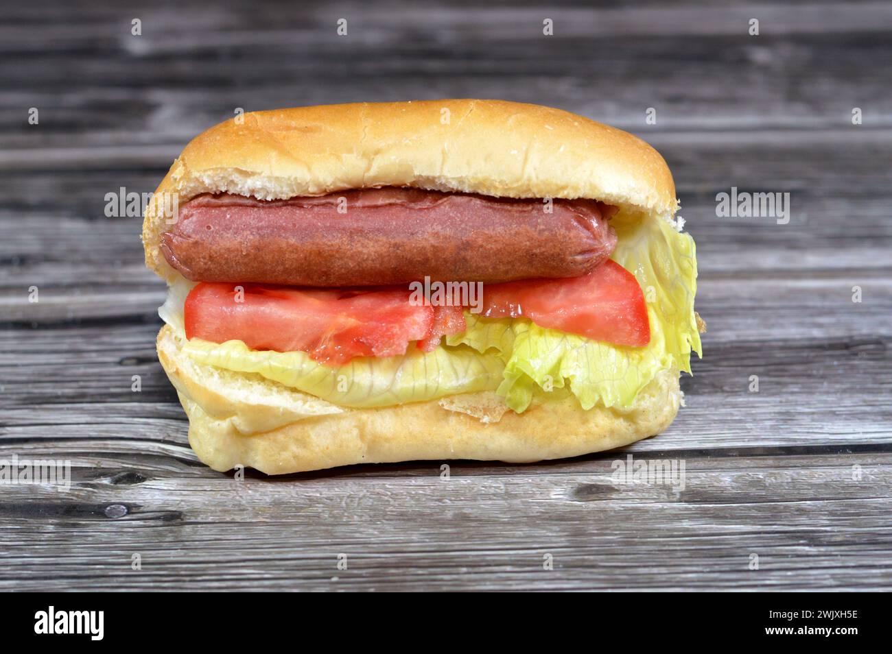 Hot dog in panino con lattuga e fette di pomodoro, salsiccia di manzo grigliata chiamata wiener (salsiccia viennese) e frankfurter frank con lattuga e pomodoro, dentro Foto Stock